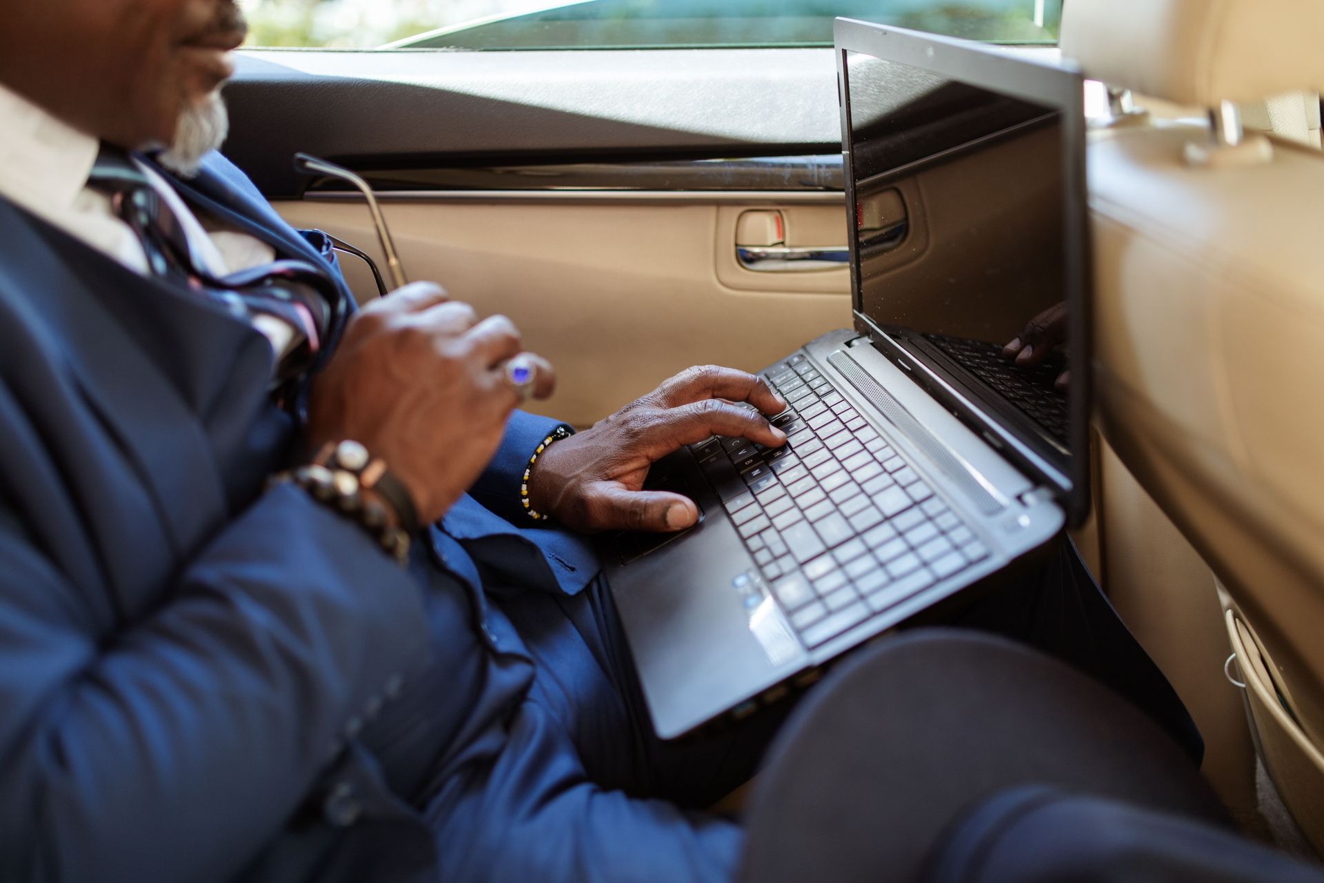 Close-up of a businessman typing on a laptop in a car interior during travel.